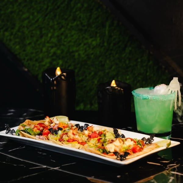 Halloween-themed flatbreads with bat decorations and a green cocktail with a spooky eyeball and hand.