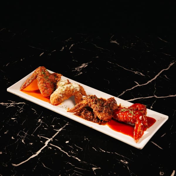 Four different flavors of chicken wings on a long white plate, on a black marble surface.