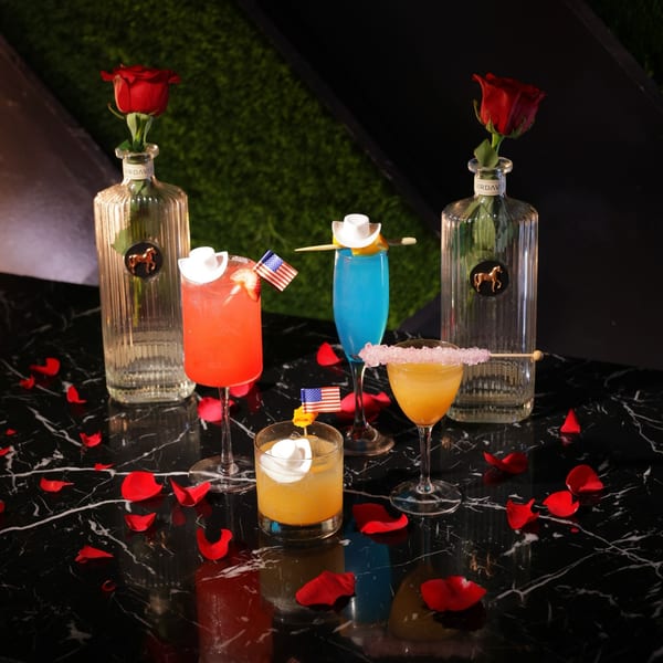 Four colorful cocktails with festive garnishes and rose petals on a black marble table.