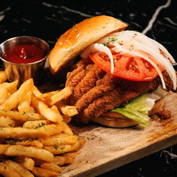 Crispy fried fish sandwich with lettuce, tomato, and onions, served with fries and ketchup.